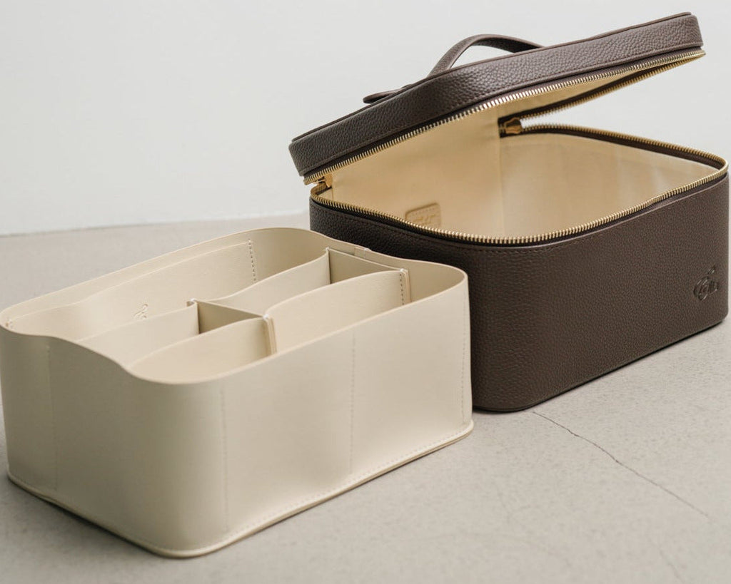 Two cosmetic boxes, one beige and one brown, on a light gray surface with a white background.