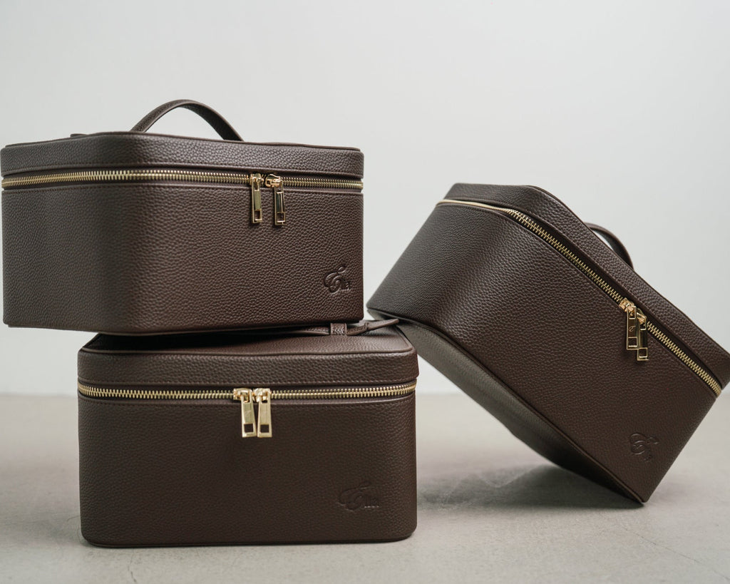Three brown cosmetic bags with gold zippers on a light gray background
