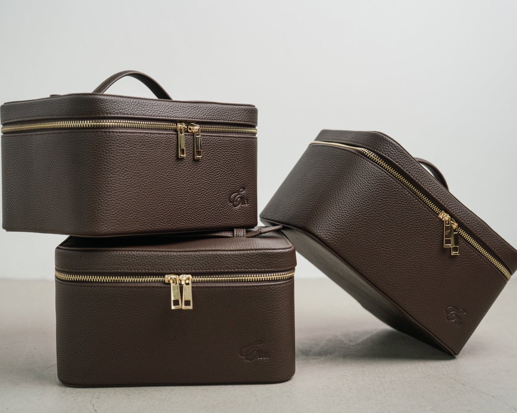 Three brown cosmetic bags with gold zippers on a light gray background