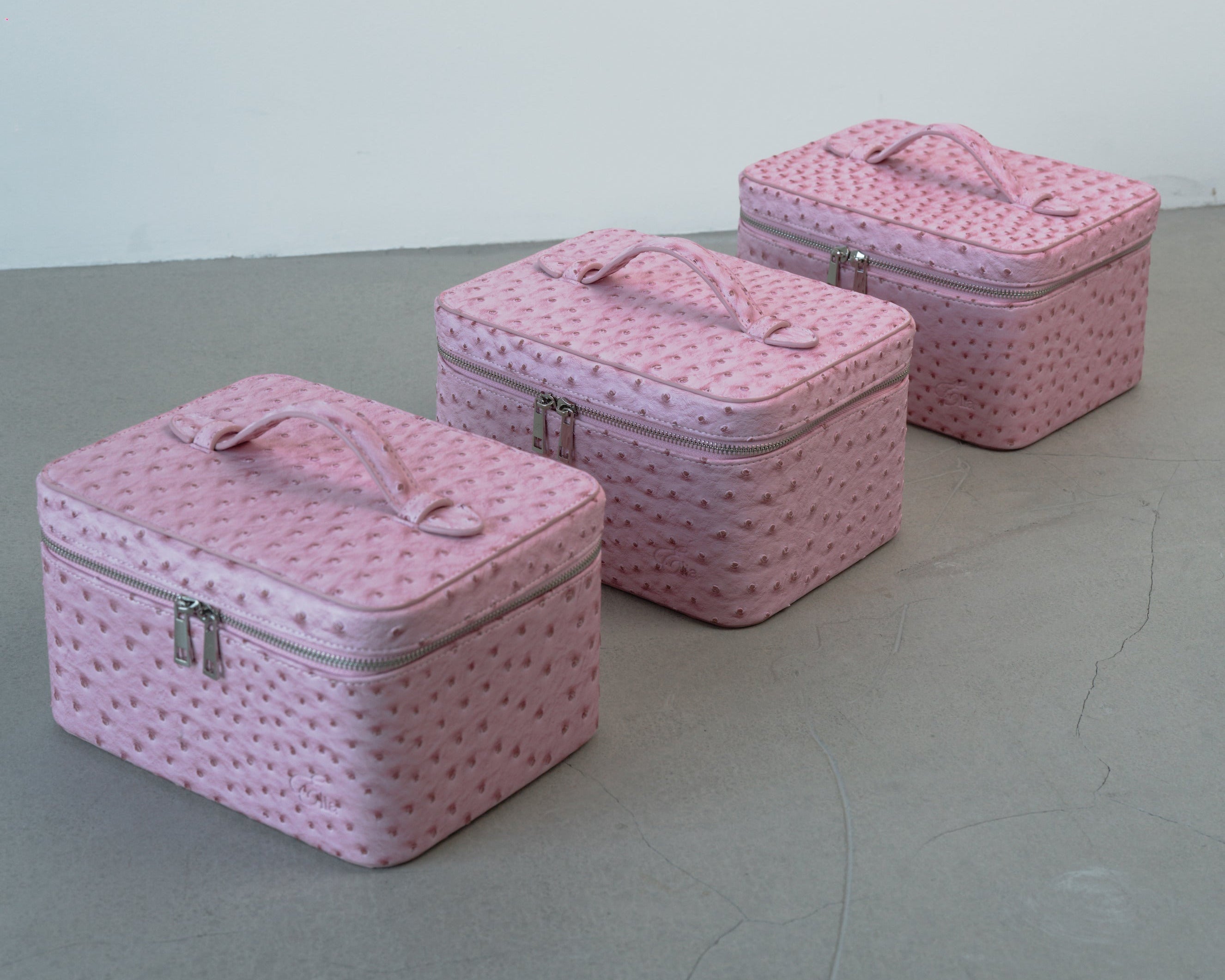 Set of three pink textured cosmetic cases on a gray surface with a white background